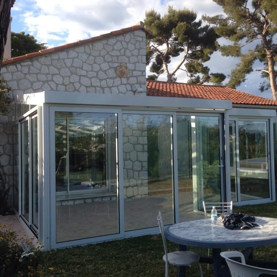 Veranda in alluminio bianco con grandi vetrate scorrevoli accanto a una casa in pietra